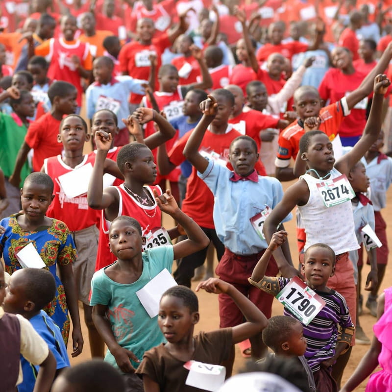 Hundreds of children with race bibs cheer with raised fists at the Kyotera Women's Health Charity Run, the annual community event DROTY organizes with local government partners.