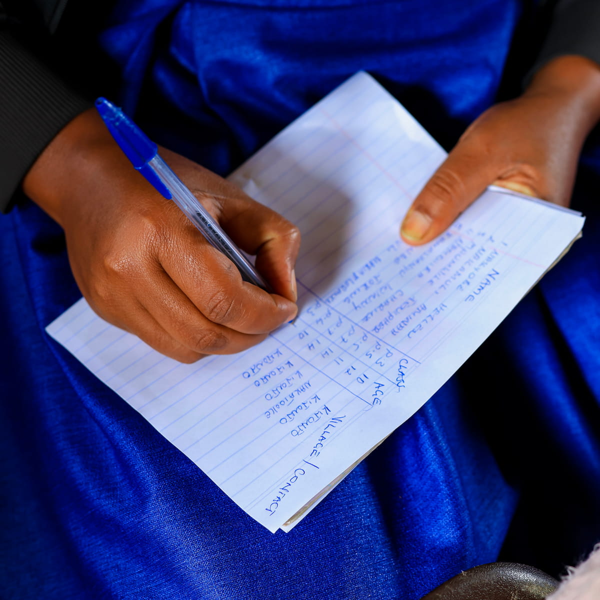 A DROTY participant records names, ages, and villages of attendees in a notebook during a community session.
